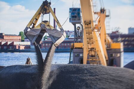 Bulk-handling crane unloading sand, road metal and gravel from cargo vessel ship, heavy vehicle and portal crane loader working with bulk materials in dock terminalの写真素材
