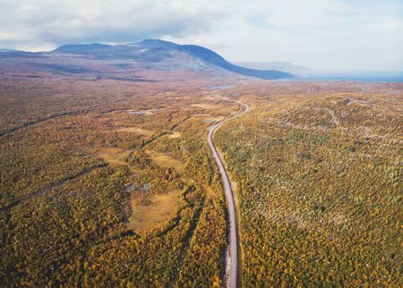 Aerial sunny fall autumn view of Abisko National Park, Kiruna Municipality, Lapland, Norrbotten County, Sweden, shot from drone, with Abiskojokk river, road and Nuolja mountainの写真素材