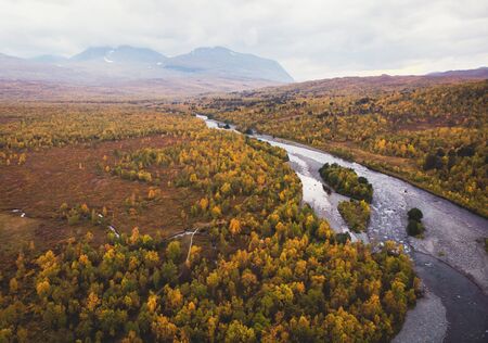 Aerial sunny fall autumn view of Abisko National Park, Kiruna Municipality, Lapland, Norrbotten County, Sweden, shot from drone, with Abiskojokk river, road and Nuolja mountainの写真素材