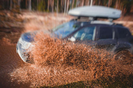 Suv offroad 4wd car rides through muddy puddle, off-road track road, with a big splash, during a...