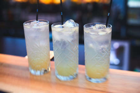 Beautiful row of different colored alcohol cocktails on a party, martini, vodka, and others on decorated catering bouquet table on open air event with bartender in a backgroundの写真素材