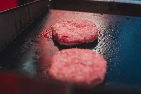 Process of cooking classic burgers with beef on open-air, view of chef hands in gloves with variety of fillings and ingredients on wooden desk and stove, summer dayの写真素材