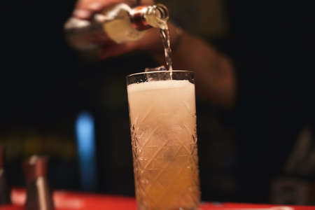 Beautiful row of different colored alcohol cocktails on a party, martini, vodka, and others on decorated catering bouquet table on open air event with bartender in a backgroundの写真素材