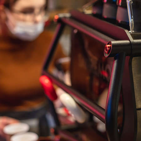 View of female barista working at coffee machine in coffee house bar, barista wearing respirator...