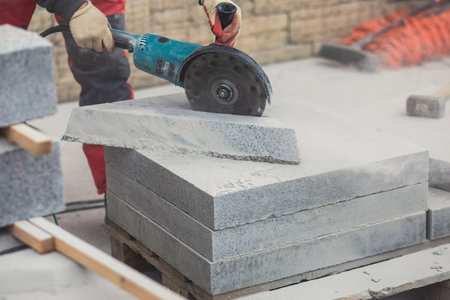 Process of cutting, sawing and grinding granite cement tile slab with cutting machine, worker with circular saw during new walkway asphalt pavement works, worker cuts a ceramic concrete tileの写真素材