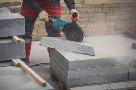 Process of cutting, sawing and grinding granite cement tile slab with cutting machine, worker with circular saw during new walkway asphalt pavement works, worker cuts a ceramic concrete tileの写真素材