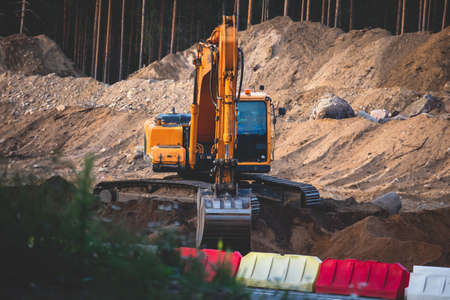 Yellow heavy excavator and bulldozer excavating sand and working during road works, unloading sand during construction of new roadの写真素材