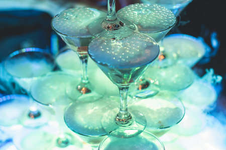 Pyramid of glasses with alcoholic beverages, filling and pouring beautiful pyramid line of different colored alcohol cocktails with champagne and dry ice on a party, catering banquetの写真素材