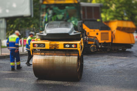 Process of asphalting, blacktopping and paving, asphalt paver machine and steam roller compactor during construction and repairing works, workers on construction site, rental vehicle workingの写真素材