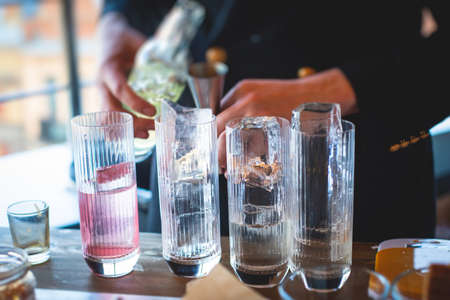 Bartender in front of beautiful row of different colored alcohol cocktails on a party in a nightclub bar, martini, vodka, and others on decorated catering banquet table on open air eventの写真素材