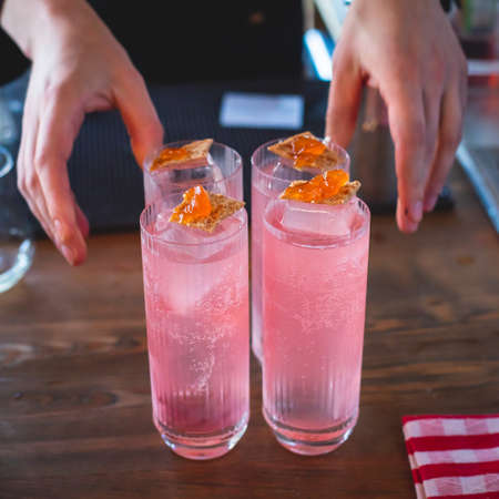 Bartender in front of beautiful row of different colored alcohol cocktails on a party in a nightclub bar, martini, vodka, and others on decorated catering banquet table on open air eventの写真素材