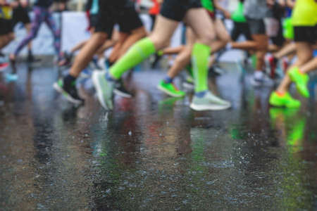 Marathon runners competition in the rain close-up, view of footwear running shoes during half-marathon on the city asphalt streets with water splash, crowd of joggers in motion, outdoor trainingの写真素材