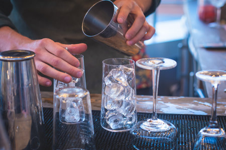 Bartender in front of beautiful row of different colored alcohol cocktails on a party in a nightclub bar, martini, vodka, and others on decorated catering banquet table on open air eventの写真素材
