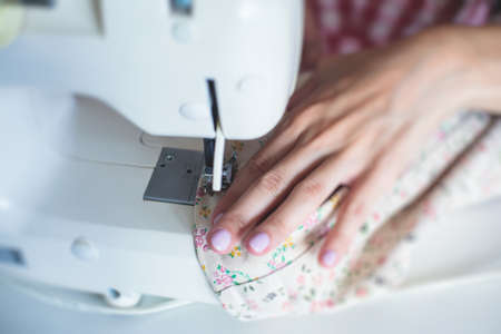 Process of hemming the dress and pants at home, close up of cloth on the sewing machine, hemming, tailoring, repairing and stitching cloth and dress, with the hand of female dressmakerの写真素材