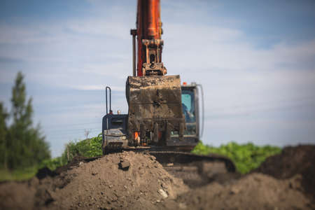 Yellow heavy excavator and bulldozer excavating sand and working during road works, unloading sand during construction repair of the new roadの写真素材