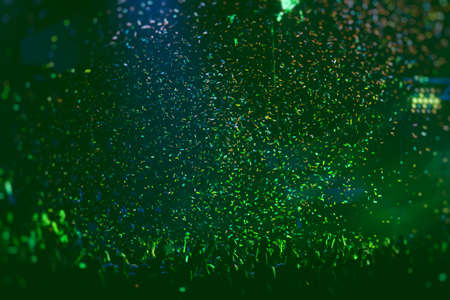A crowded concert hall with scene stage green lights, rock show performance, with people silhouette, confetti explosion fired on dance floor air during a concert festivalの写真素材