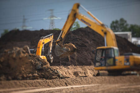 Yellow heavy excavator and bulldozer excavating sand and working during road works, unloading sand during construction repair of the new roadの写真素材
