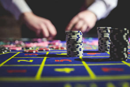 A close-up vibrant image of multicolored casino table with roulette in motion, with casino chips. the hand of croupier, money and group of gambling rich wealthy people playing in the backgroundの写真素材