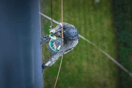 Professional climber rope access worker painting and repairing the facade of residential high rise...