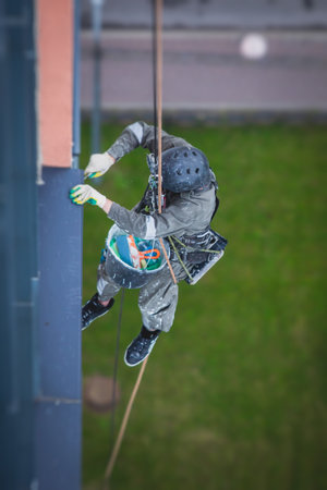 Professional climber rope access worker painting and repairing the facade of residential high rise...