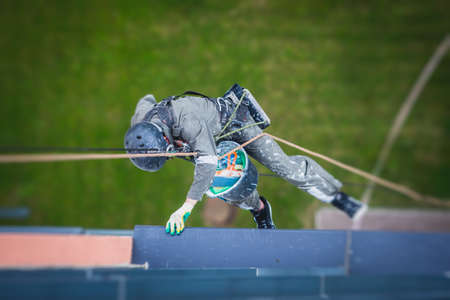 Professional climber rope access worker painting and repairing the facade of residential high rise...