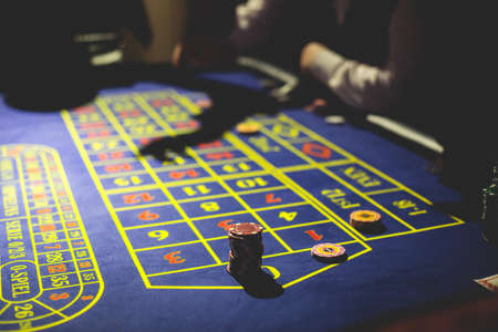 A close-up vibrant image of multicolored casino table with roulette in motion, with casino chips. the hand of croupier, money and group of gambling rich wealthy people playing in the backgroundの写真素材