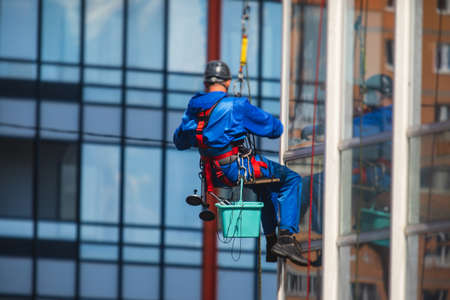 Professional climber rope access worker cleaning the windows on the high rise building, industrial...