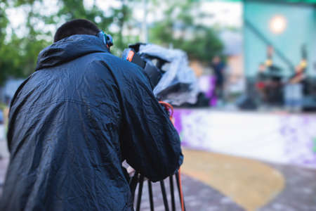 View of a camera man operator working during tv reportage, online broadcasting of concert, professional videographer with camera filming live event, rainy dayの写真素材