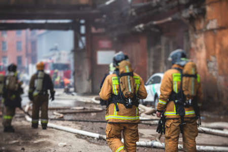 Firefighters put out large massive fire blaze, group of fire men in uniform during fire fighting operation in the city streets, firefighters with fire engine truck fighting vehicleの写真素材