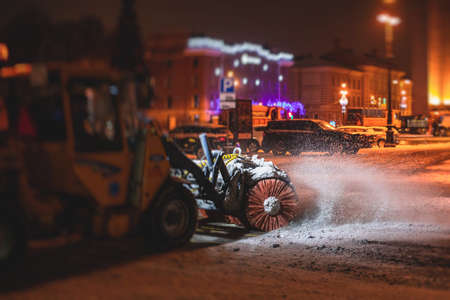 Process of snow removal on the city streets and roads with municipal vehicle, bulldozer, snowblower plow truck, snowplow, snow removal equipment in winter snowy nightの写真素材