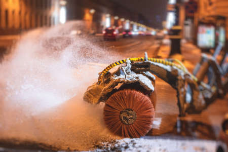 Process of snow removal on the city streets and roads with municipal vehicle, bulldozer, snowblower plow truck, snowplow, snow removal equipment in winter snowy nightの写真素材
