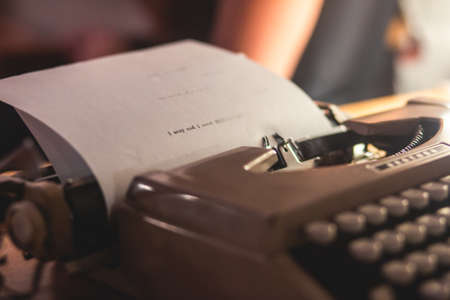 Process of writing a text letter on a white sheet of paper with old-fashioned typewriter, modern writer machine in warm room candle light, close up view of hands writing and printingの写真素材