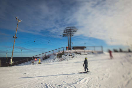 Beautiful cold mountain view of ski resort, sunny winter day with slope, piste and ski lift, with a group of mountain downhill skiers and snowboardersの写真素材