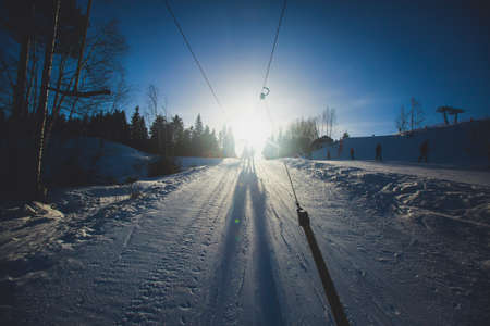 Beautiful cold mountain view of ski resort, sunny winter day with slope, piste and ski lift, with a group of mountain downhill skiers and snowboardersの写真素材