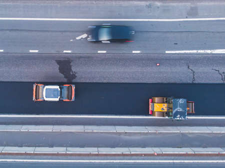 Asphalt paver machine and steam road roller during road construction and repairing works, process of asphalting and paving, workers working on a new road construction site, placing a layer, droneの写真素材