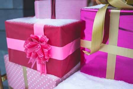 Pile of a colorful pink and golden gift boxes covered in snow near store and cafe, christmas outdoor display shop front decoration, boutique outside new year decorの写真素材