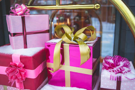 Pile of a colorful pink and golden gift boxes covered in snow near store and cafe, christmas outdoor display shop front decoration, boutique outside new year decorの写真素材