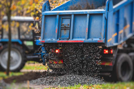 Dump truck, tractor and bulldozer unloading gravel, road metal, rubble and crushed stone cement material during landscaping improvement and new pedestrian walk path road construction siteの写真素材