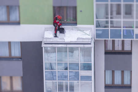 Professional climber rope access worker with a shovel removes snow and take off icicle from high rise building, industrial mountaineers working at heights, manual snow removal, cleaning roofsの写真素材