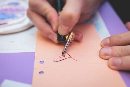 Process of calligraphy handwriting with an ink fountain pen feather, calligrapher practicing writing on postcard paper using pen brush and sign pen with inkwell on master-class lesson, hands viewの写真素材