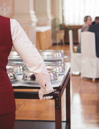 Process of serving luxury dinner in a cloche plate dish with a lid, waiter serving main course meal under silver platter on a banquet in a restaurant or hotel, serving dish food coverの写真素材