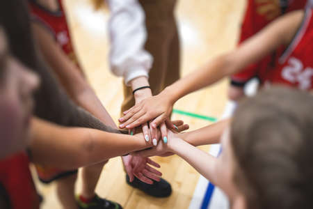Team of kids children basketball players stacking hands in the court, sports team together holding hands getting ready for the game, playing indoor basketball, team talk with coach, close up of handsの写真素材