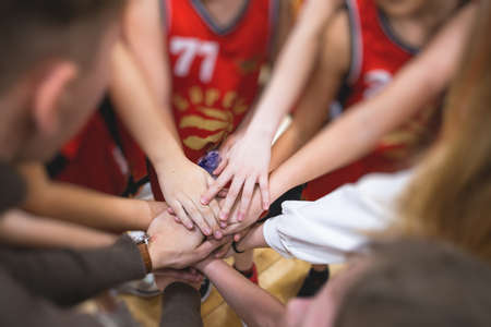 Team of kids children basketball players stacking hands in the court, sports team together holding hands getting ready for the game, playing indoor basketball, team talk with coach, close up of handsの写真素材