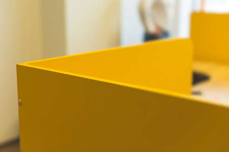 View of modern office space interior with desks in yellow tones with workers, employee with a laptop...