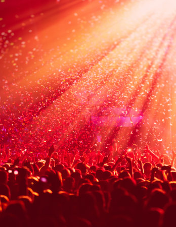 A crowded concert hall with stage stage in red lights, rock show performance, with people silhouette, colorful confetti explosion fired on dance floor during a festival concertの写真素材