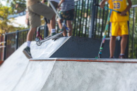 Skate park view with kids on a kick scooter doing tricks and stunts, boys in a skate park riding bmx bike and skate, playing and enjoying summer on a new ramp, teenagers skateboarders and bmx ridersの写真素材