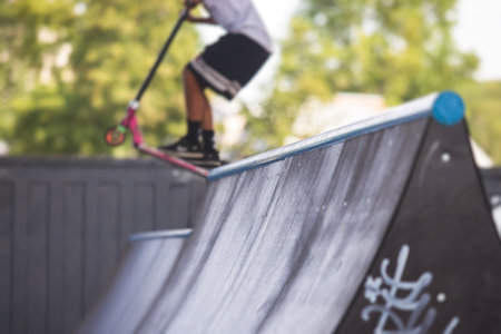 Skate park view with kids on a kick scooter doing tricks and stunts, boys in a skate park riding bmx bike and skate, playing and enjoying summer on a new ramp, teenagers skateboarders and bmx ridersの写真素材