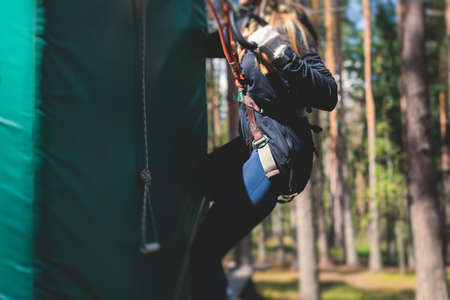 View of high ropes course, process of climbing in amusement acitivity rope park, passing obstacles and zip line on heights in climbing safety equipment gear between the trees, summer dayの写真素材