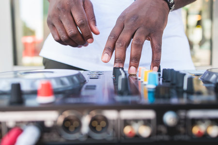 View of Dj mixer and vinyl plate with headphones on a table with african american DJ playing on stage and mixes the track in the background, during summer open air event techno party, hand close-upの写真素材