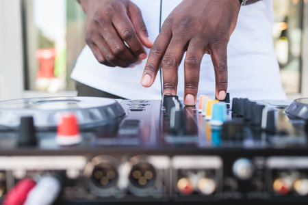 View of Dj mixer and vinyl plate with headphones on a table with african american DJ playing on stage and mixes the track in the background, during summer open air event techno party, hand close-upの写真素材